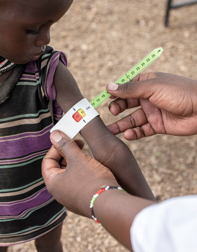 A child being examined at a medical site using MUAC tape by IRC staff member to assess malnutrition.